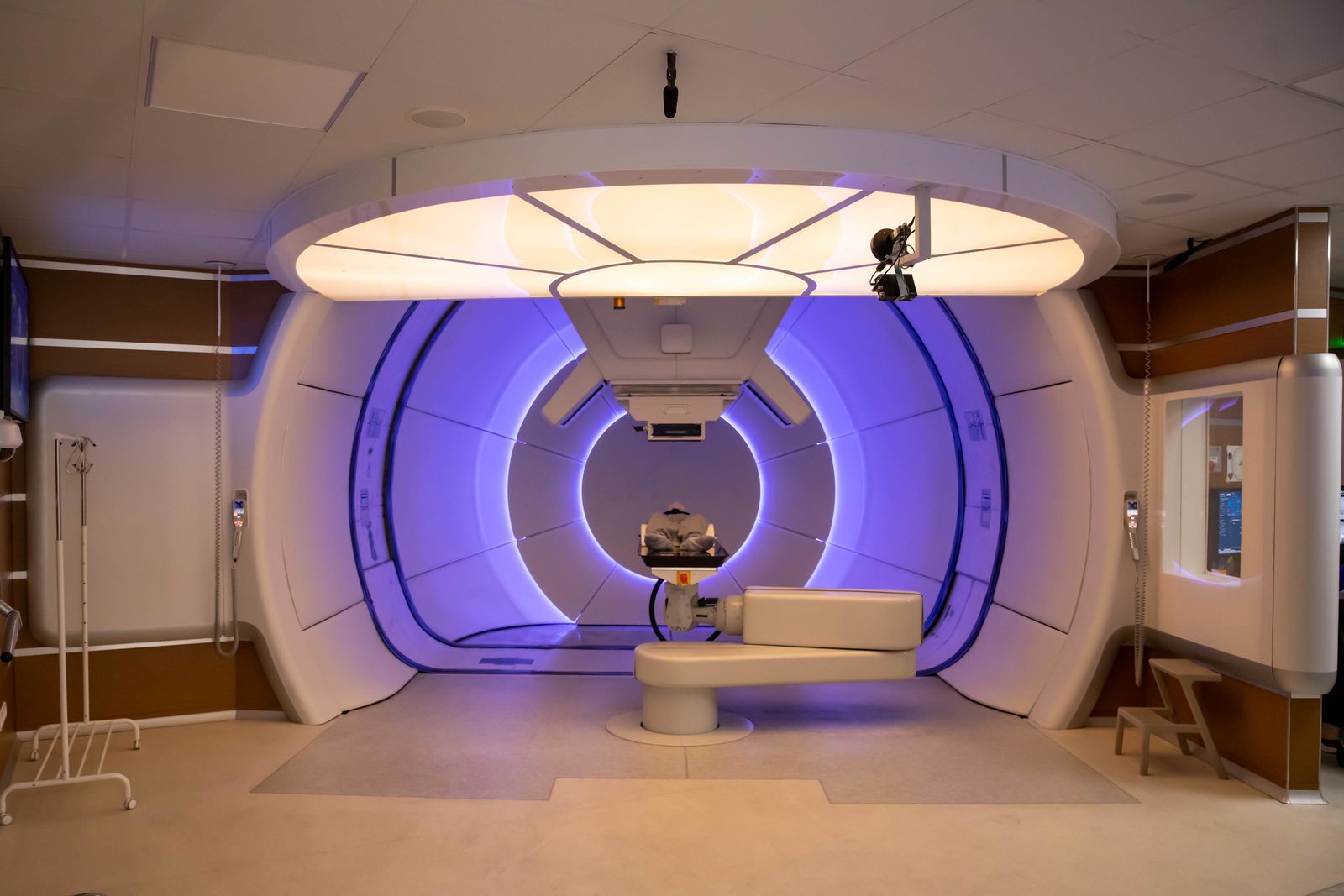 A proton therapy treatment room: the gantry and beam nozzle surround the patient couch under purple light