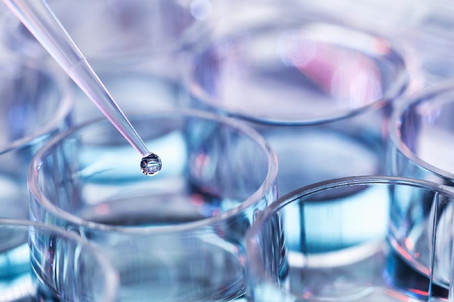 A close up of an eye dropper putting liquid in a glass vessel
